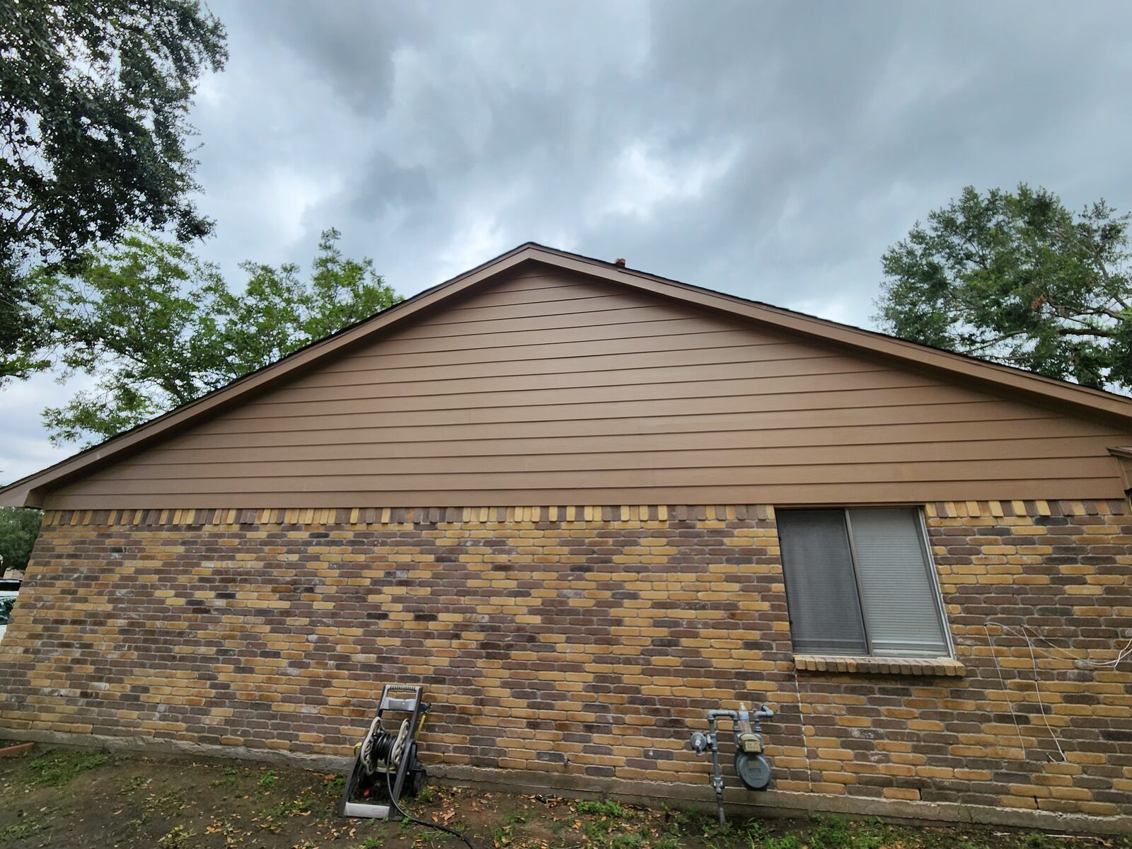 Brown painted gable siding above brick on a Houston home