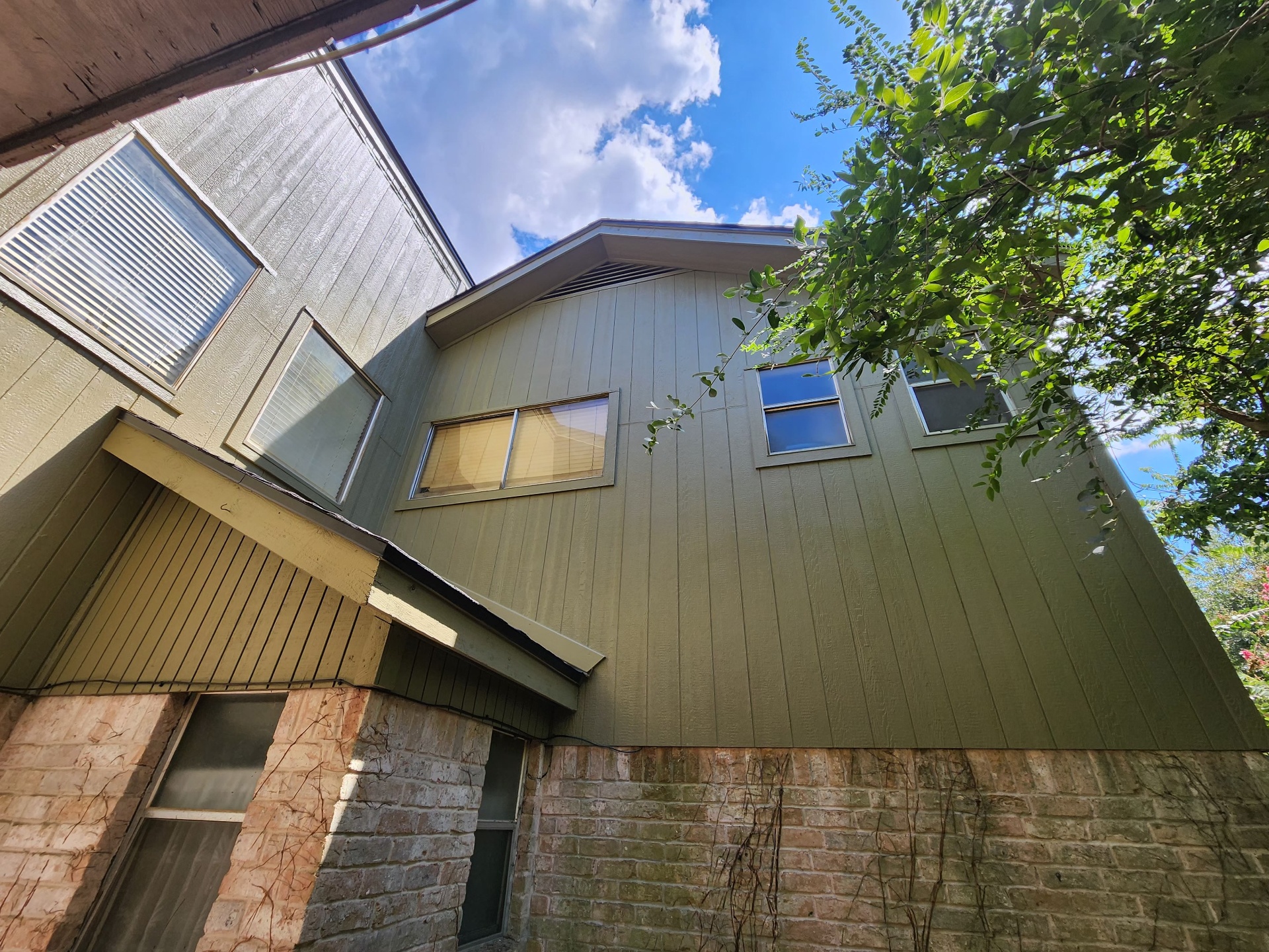 Freshly painted green siding and trim above brick on a two story Houston home